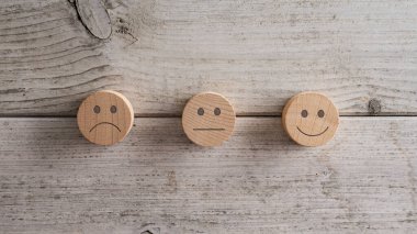 Üç ahşap kesim çemberi, her birinde farklı bir ifade var. Hüzünlü, ortalama ve gülümseyen. Müşteri memnuniyeti ve reytinginin kavramsal görüntüsü. Beyaz ahşap arka planda.