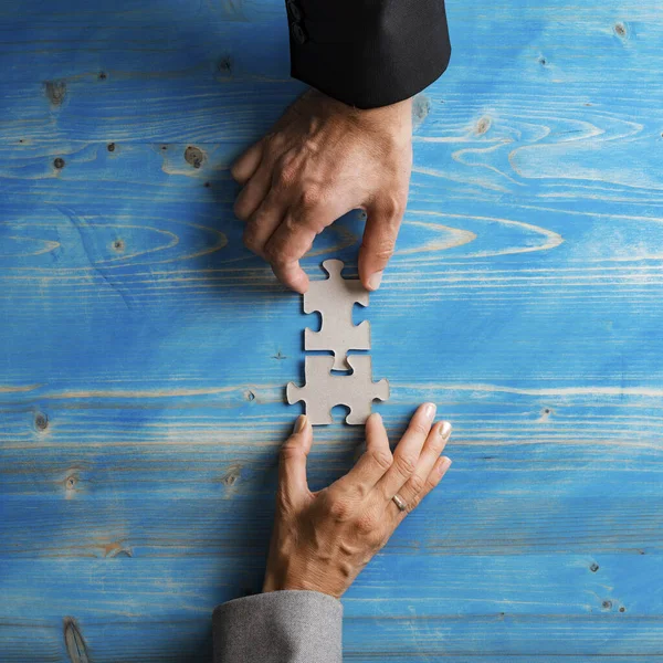 男性と女性の手のトップビューでスーツマッチングと結合二つの空白のパズルピース以上テクスチャブルー木製の背景 — ストック写真