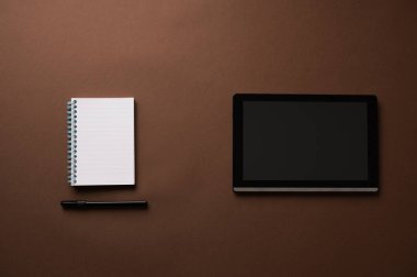 Siyah işaretli boş spiral not defteri ve kahverengi arkaplana yerleştirilmiş boş ekran dijital tableti.