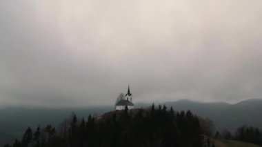 Slovenya 'daki St. Jakob kilisesinin etrafında dönen bir İHA ile sakin sakin bir sabah bulutlu bir tepede çekilmiş görüntüler..