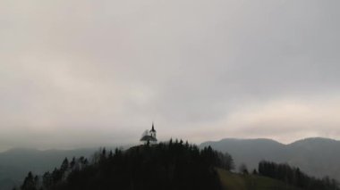 Medvode, Ljubljana, Slovenya 'daki bir tepedeki St. Jakob kilisesinden hareket eden bir İHA' nın hava görüntüsü. Sakin bulutlu bir sabahta.