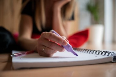 Low angle closeup view of female hand about to highlight something in her notebook with a purple marker. Student learning and studying.