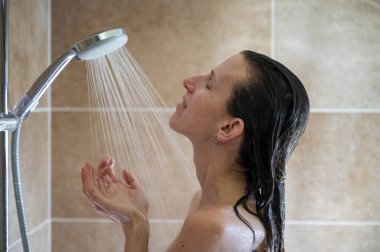 Profile view of a young woman, a brunette, taking a shower washing her hair. 