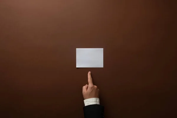 メモ又は茶色の背景の上に置かれたメモのために準備ができている紙切れを指しているビジネスマンの手 — ストック写真