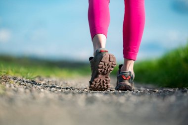 Çakıl yolunda yürürken ayakkabının tabanının alçak açılı görüntüsü. Pembe bacaklı bir kadının dışarıda aktif olması..