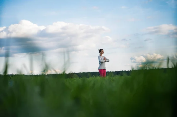 宁静的年轻女子站在蓝天的阴云下 手心紧握着胸前的绿草 透过低矮的视角看风景 — 图库照片
