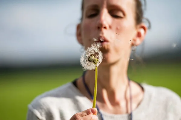 種が空気中に飛び込むためにタンポポの球根を吹いて若い女性 — ストック写真
