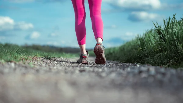 穿着粉红腿 慢跑者或远足者的女性腿的低角度视图 在穿过绿地的砾石乡间道路上迈进一步 — 图库照片