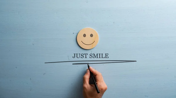 男性的手在一个木制切割圆圈下写下一个微笑标志 上面画着一张笑脸 在浅蓝色的木制背景上 有复制空间 — 图库照片