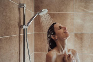 Uzun bir günün ardından sıcak bir duş almak isteyen genç bir kadın. Şampuanlı saçlarında su akıyor..