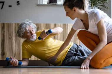 Kişisel antrenör ya da yaşlı bir adamla çalışan bir fizyoterapist ona sağlıklı ve formda kalması için halterlerle nasıl egzersiz yapacağını öğretiyor..