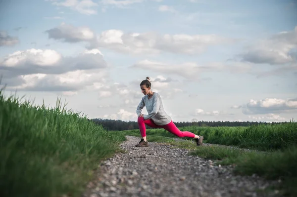 年轻女子在石子路上伸展双腿 然后在美丽的绿色大自然中慢跑 — 图库照片
