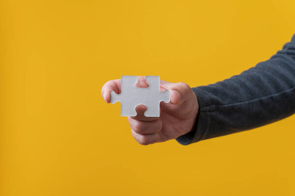 Male hand holding blank puzzle piece over bright yellow background.
