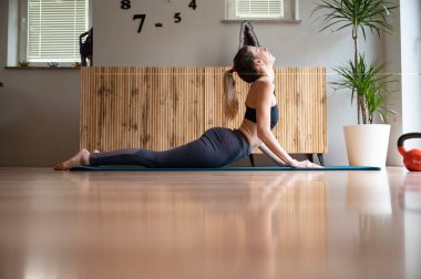 Profil görüntüsü, oturma odasındaki paspasın üzerinde egzersiz yapan, kendini yukarı kaldıran genç bir kadının profili..