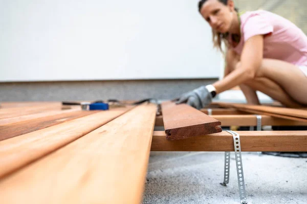 Low angle view of a woman in a home diy project placing plank of wood on a foundation framework for a new wooden patio.