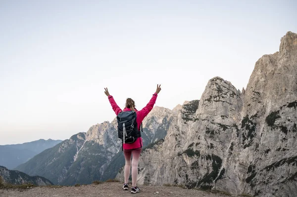 Happy woman hiking in scenic mountain landscape, standing with her arms raised high.