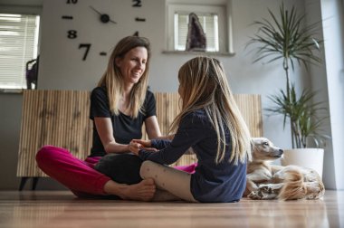 Genç anne, küçük kızıyla el oyunları oynarken evcil köpekleriyle oturma odalarının zemininde oturuyorlar..