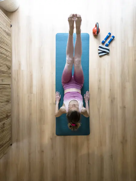 Overhead view of a fit young woman working out at home on pilates or yoga mat. Leaning on her elbows with legs lifted for strong abs.