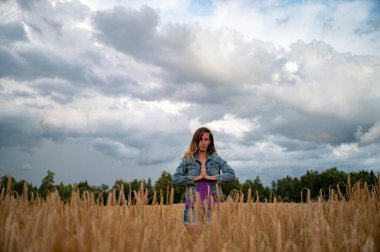 Güzel bir altın buğday tarlasında durup dua eden, avuçlarını göğsünün ve gözlerinin önünde birleştirerek meditasyon yapan ya da pratik yapan sakin bir genç kadının düşük açılı görüntüsü.. 