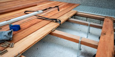 Görüntü, tahta güverte tahtalarını yerleştirmek için kullanılan gizli bir bağlama sisteminin yakın çekimini yakalıyor. Sahnede vidalar, bağlama klipsleri ve yanında dinlenen iş eldivenleri yer alıyor. Odak noktamız tahtaların kesin hizalanması, 