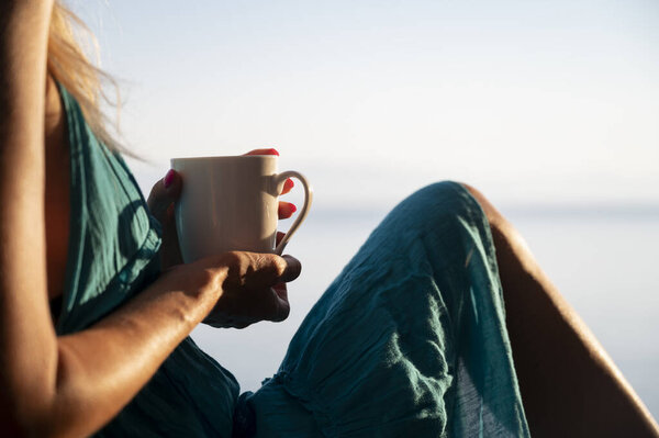 A person relaxes, holding a coffee cup, bathed in warm sunlight. The serene setting and peaceful moment emphasize a quiet escape, dressed in a flowing teal outfit.