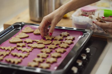 Bir insan kurabiye hamurunu çeşitli şekillerde düzenler. Yıldızlar ve kalpler de dahil. Pembe silikon bir hasırla kaplanmış, pişirilmeye hazır bir tepside..
