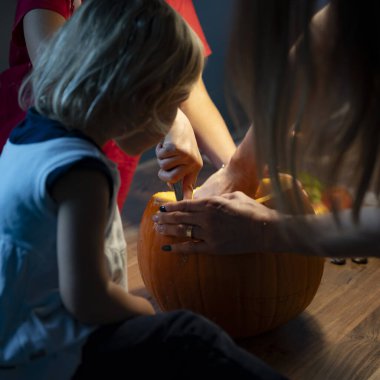  Bir çocuk dikkatle izlerken balkabağını oyan yakın plan bir el. Sahne, Cadılar Bayramı hazırlığının sıcak bir anını yakalıyor..