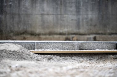 Çakıl taşı, beton bloklar ve ahşap bir tahtanın bulunduğu bir inşaat sahasının yakınına. Vakıf çalışmalarının ilk aşamalarını sergiliyor..