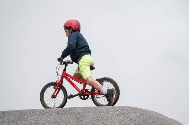 Kırmızı kask takan bir çocuk kayalık bir arazide kırmızı bir bisiklete biniyor, keşif yapıyor ve dışarıda eğleniyor.