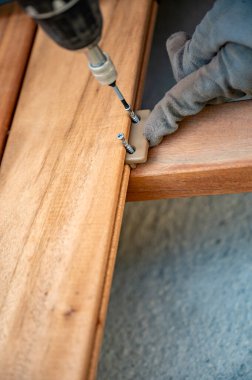 Eldivenli bir elin, matkap ve vida kullanarak ahşap bir kalası emniyete alırken, montajda istikrar ve hassasiyet sağladığı yakın plan..