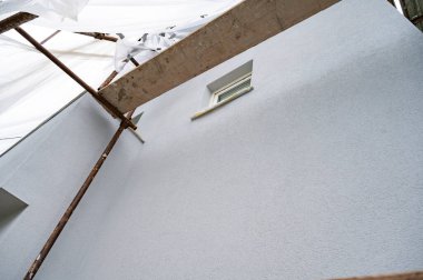 İnşaat iskelesi ve koruyucu plastik kaplama ile yenilenmiş yeni boyanmış ve boyanmış bir binanın yakın çekim görüntüsü.