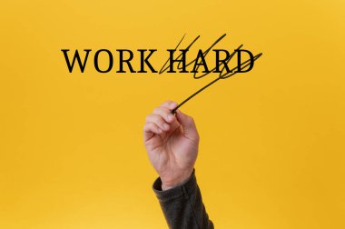Daha akıllı ve verimli çalışma stratejilerine doğru kaymayı sembolize eden, parlak sarı arka planda bir işaretle Sıkı Çalışın 'ın üstünü çizen bir el..