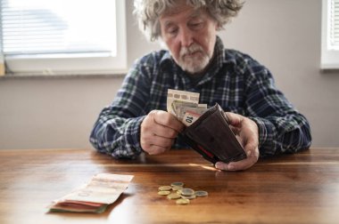 Yerel masada oturan otantik kıdemli bir adam cüzdanında ne kadar emekli maaşı kaldığını sayıyor. Masasında paralar ve banknotlar var..