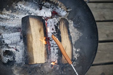 Bir sosisli, yanan odunlar ve parlayan közlerle çatırdayan bir ateş çukurunda kızartılıyor..