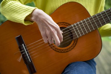 Parlak sarı bir kazak giyen, akustik gitar çalan, müziğin sıcaklığını yakalayan ve rahatlatıcı bir an yaşayan birinin yakın çekimi..