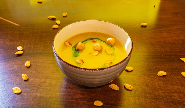 Small bowl of pumpkin cream soup with puffs and pumpkin seeds and parsley oil