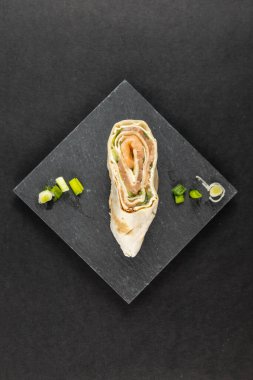 Krem peynirli lavaş tortilla atıştırmalıkları füme somon ve soğan süslemeli taş tabakta salatalık.