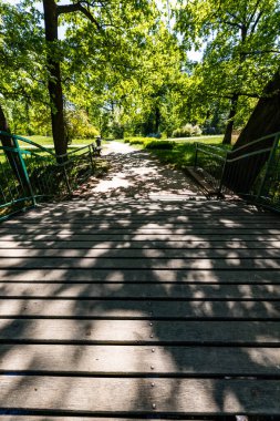 Old renovated retro bridge with green metal railings over small river in small colorful park at sunny morning
