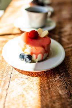 Colorful small fruity cupcakes on small white plates and cups of black coffee on wooden structure background