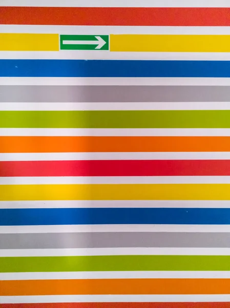 Wall full of colorful horizontal lines and green arrow as direction of escape route