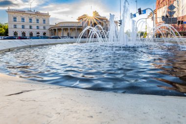 Wroclaw, Polonya - Haziran 2022: Kavşağın ortasında küçük bir çeşme Swiebodzki tren istasyonunun önünde, arkasından parlayan bir güneş doğar