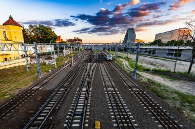 Poznan, Polonya - Temmuz 2022: Tren raylarındaki Teatralny Köprüsü manzarası, hareket eden trenler ve gün batımında şehrin ufuk çizgisi