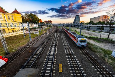 Poznan, Polonya - Temmuz 2022: Tren raylarındaki Teatralny Köprüsü manzarası, hareket eden trenler ve gün batımında şehrin ufuk çizgisi