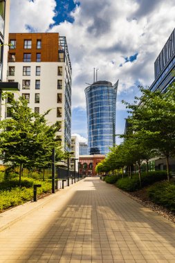 Varşova, Polonya - Temmuz 2022: Şehrin ortasında uzun Varşova Spire gökdeleniyle bloklar, çalılar ve alçak ağaçlar arasında bir patika