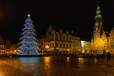 Wroclaw, Polonya - Ocak 2023: Yürüyen insanlar, parlayan fenerler ve güzel ve renkli yüksek noel ağacı ile pazar meydanı