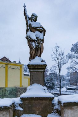Klodzko, Polonya - Ocak 2023: Mlynowka nehri üzerindeki Gotik köprünün kenarında kışın karla kaplı küçük eski bir heykel