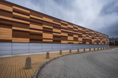 Metal ve ahşap panellerle kaplı modern binanın ön cephesi bulutlu bir öğleden sonra duvarın önünde duran kırmızı arabayla.