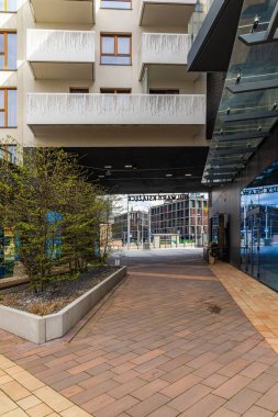 Wroclaw, Polonya - 15 Nisan 2023: Yeni malikanenin modern binaları arasında cam cepheli ve yanında ahşap banklar bulunan büyük çalılar arasında küçük bir yol
