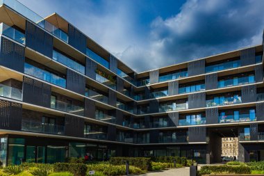 Wroclaw, Polonya - 15 Nisan 2023: New York 'ta, şehir merkezinde Odra nehrinin yanında yeşil kare ve kafeler bulunan modern apartman bloğunun karanlık ve camsı cephesi 