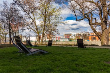 Wroclaw, Polonya - 15 Nisan 2023: Yeni modern malikanenin yanındaki yeşil meydan, Odra nehrinin yanında birkaç tahta güneşlik.